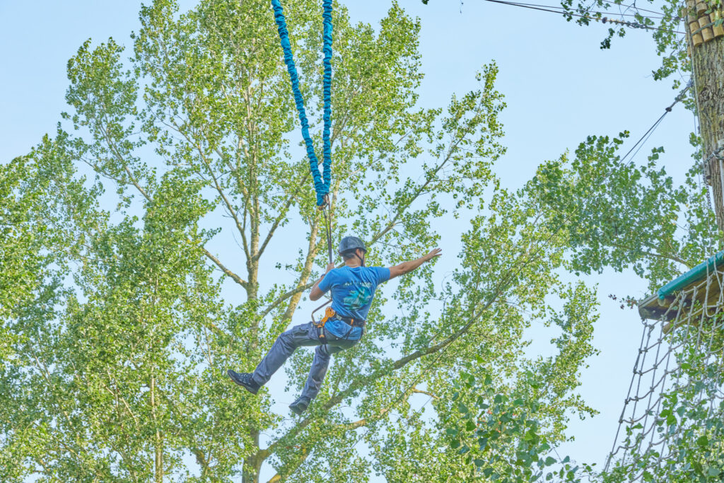 Man reikt naar het volgende platform terwijl hij vastzit aan de blauwe elastieken van de bungeejump.