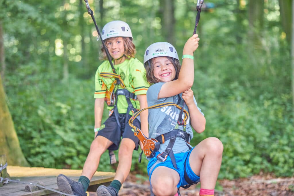 Twee kinderen hangen in hun gordels en lachen naar de camera.