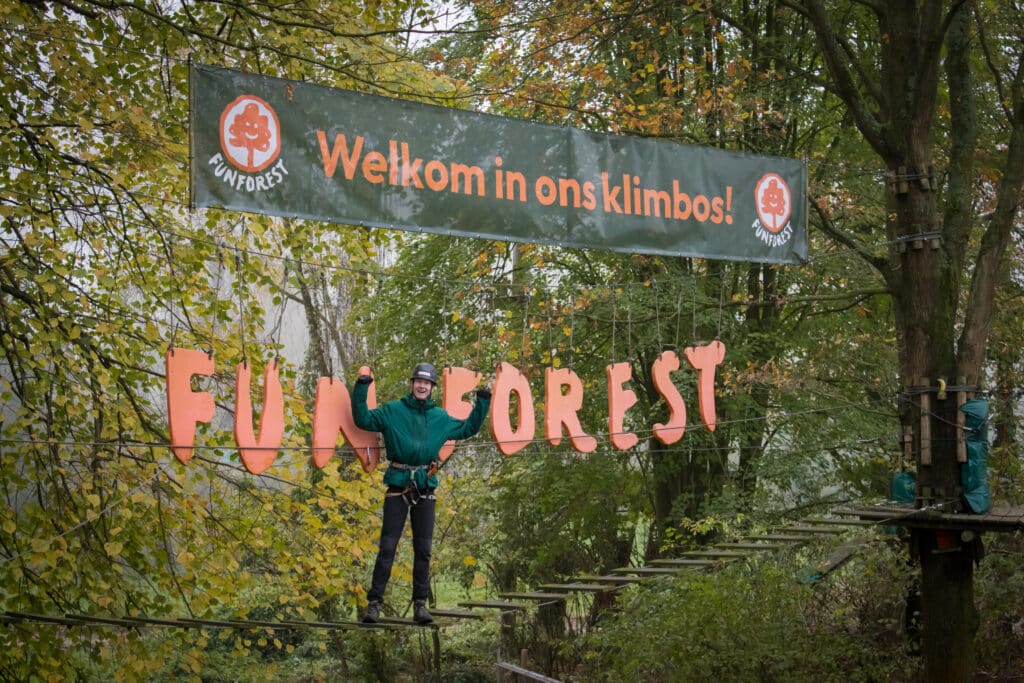 Man in groene jas staat trots op een brug tussen de Fun Forest letters in Almere. Boven hem hangt een banner met daarop de tekst "Welkom in ons bos!"